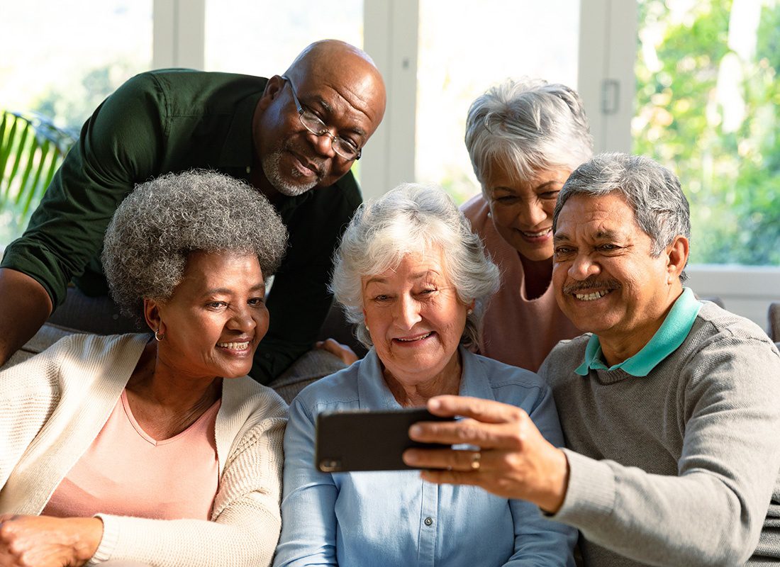 Service Center - Diverse Group of Smiling Seniors Having Fun Spending Time Together at Home While Watching a Video on a Phone